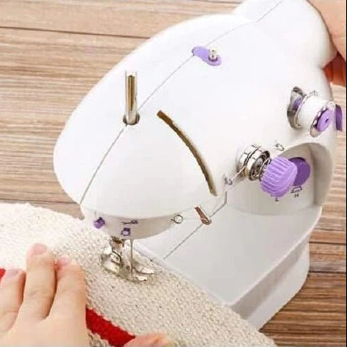 Small white sewing machine being used on a piece of fabric with red and white stripes.